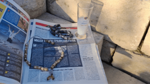 Zwei griechische Sorgenketten liegen neben einem Glas Ouzo auf einer Zeitung im Sonnenlicht. Das Komboloi ist ein Kulturgut.